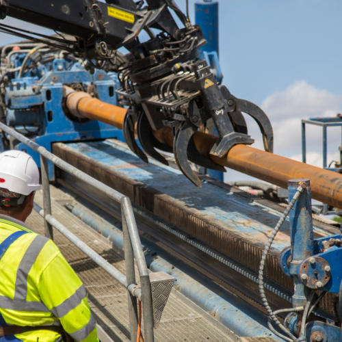 Man in yellow PPE operating a gripper for a drill rig - trenchless technologies