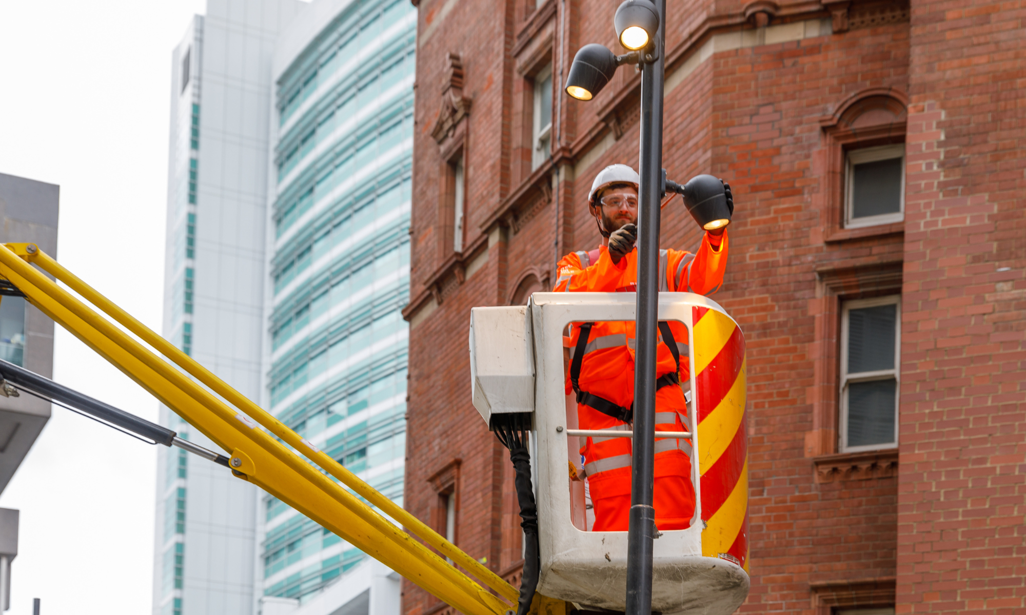 Man wearing orange PPE in a cherry pick fixing an LED street light