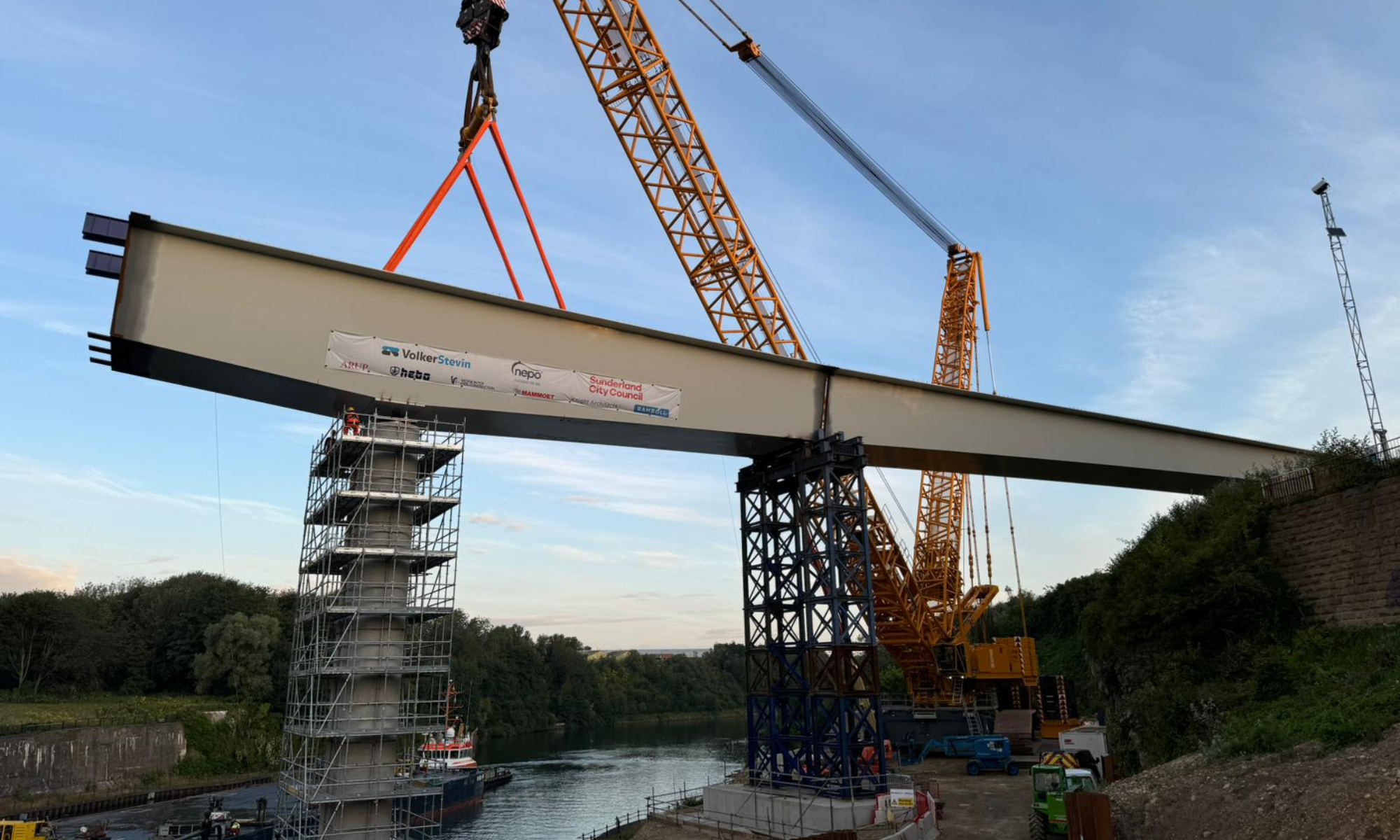 Crane lifting a section of the bridge into place on a sunny day.